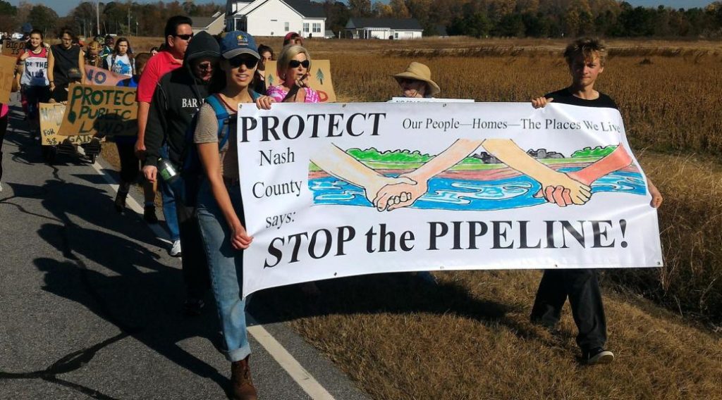 People march with a banner that says Protect our communities stop the pipeline